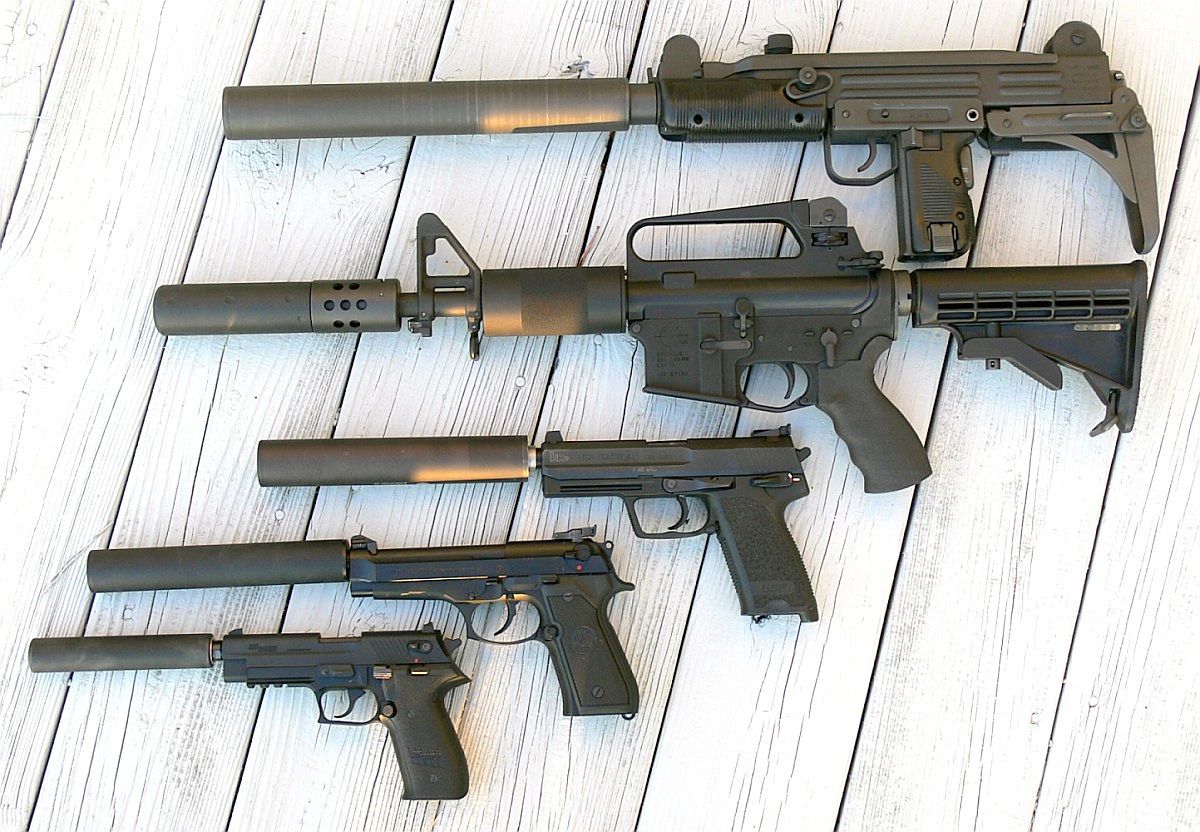 Tactical firearms with suppressors displayed on wooden background